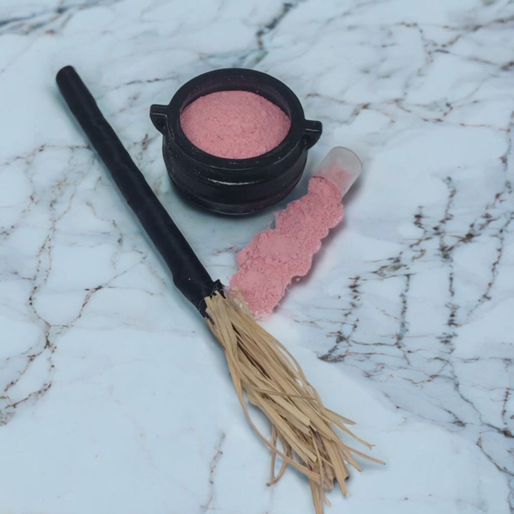 Imagem de Pó de MIronga Amor para rituais e magias, espalhado sobre base de mármore, juntamente com mini caldeiração de bruxa e mini vassoura.